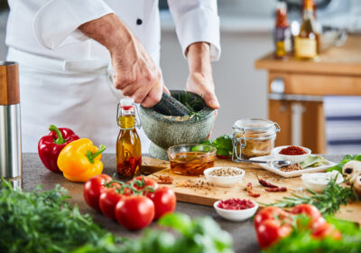 Multiple bowls of spices sitting on cutting board next to tomatoes behind leafy vegetables in foreground