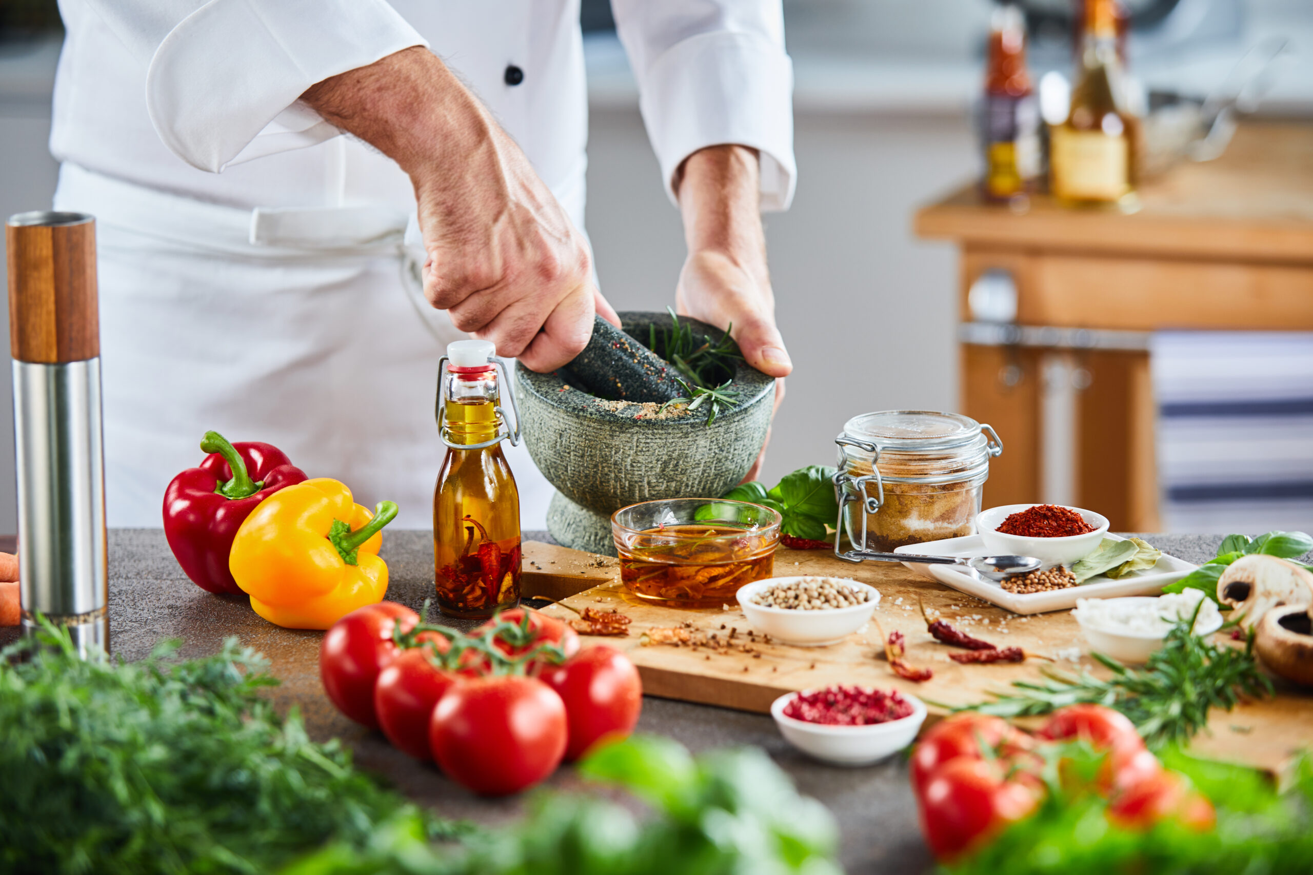 Multiple bowls of spices sitting on cutting board next to tomatoes behind leafy vegetables in foreground