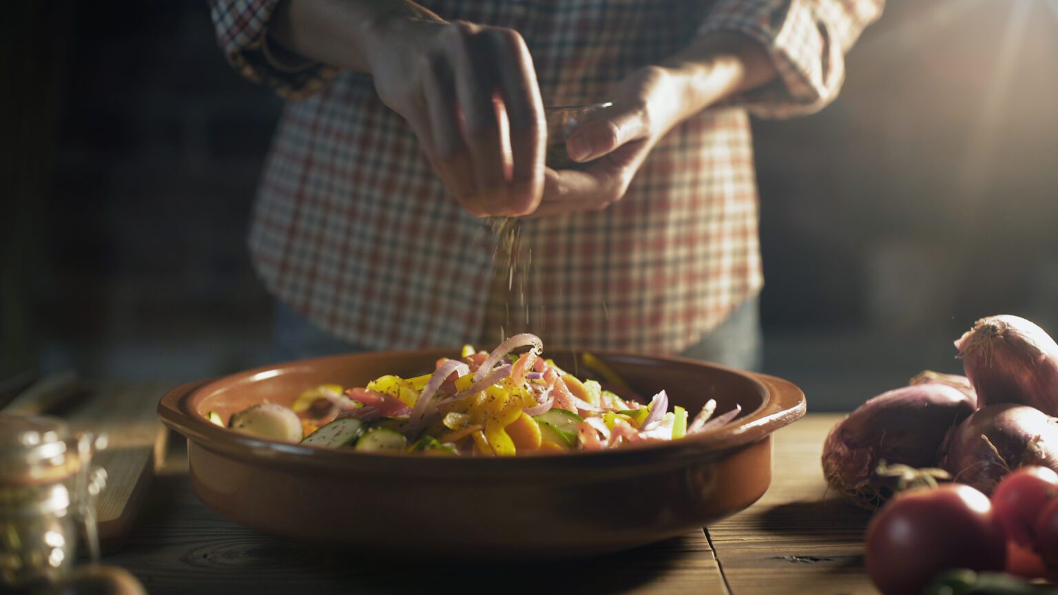 Woman preparing a healthy meal at home, she is seasoning mixed vegetables in a blow