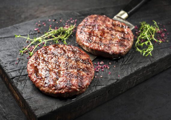 Barbecue Wagyu Hamburger with red wine salt and herbs as closeup on a charred wooden board