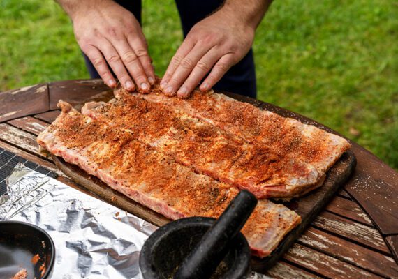 Marinated BBQ pork ribs on a wooden backyard table. Preparation process of barbeque for Grilling, Smoking, Baking and Roasting. Lifestyle concept.