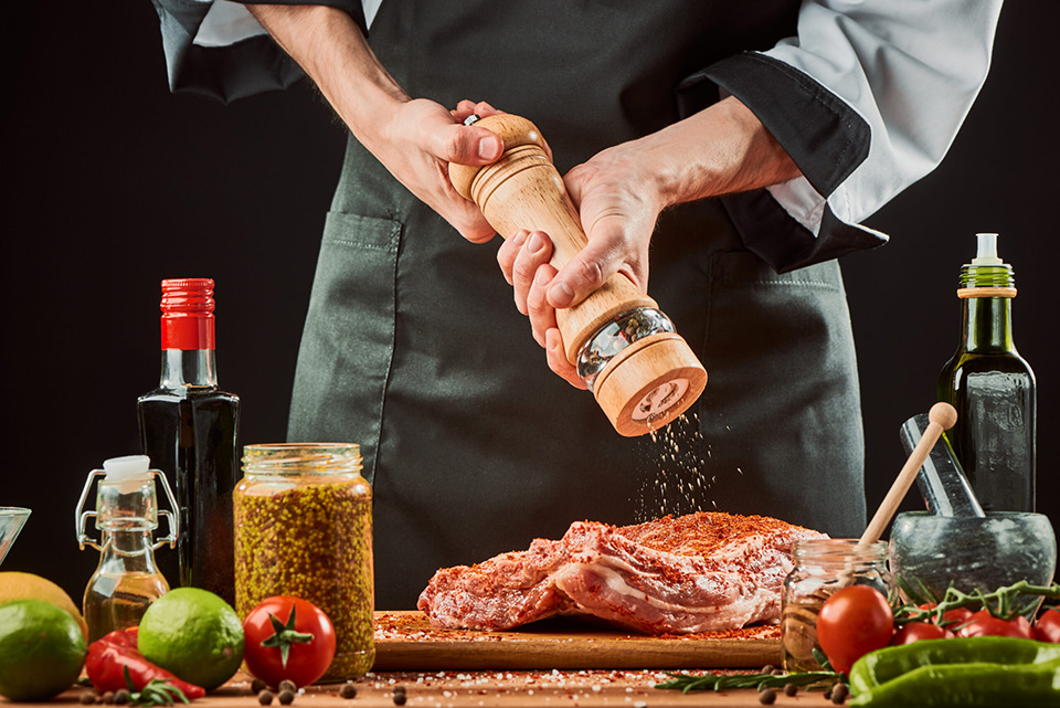 Chef grinding pepper over beef ribs. Professional cook seasoning raw meat with chili. Delicious food being cooked at a restaurant.