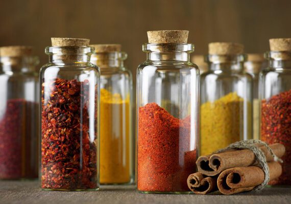 Assorted ground spices in bottles and cinnamon sticks on wood.