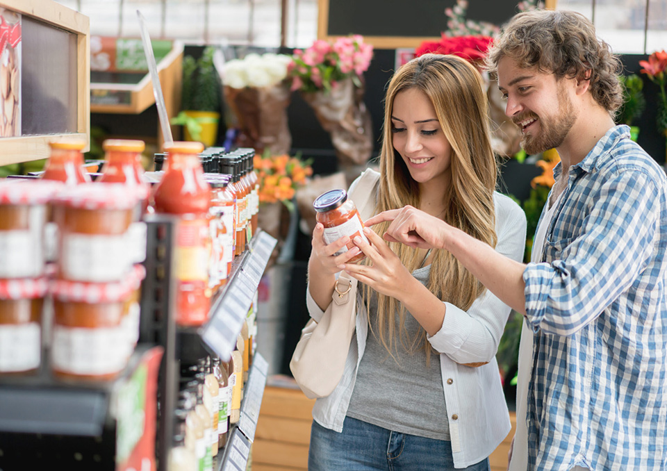 Young couple grocery shopping at the supermarket and looking at nutritional content on a jar